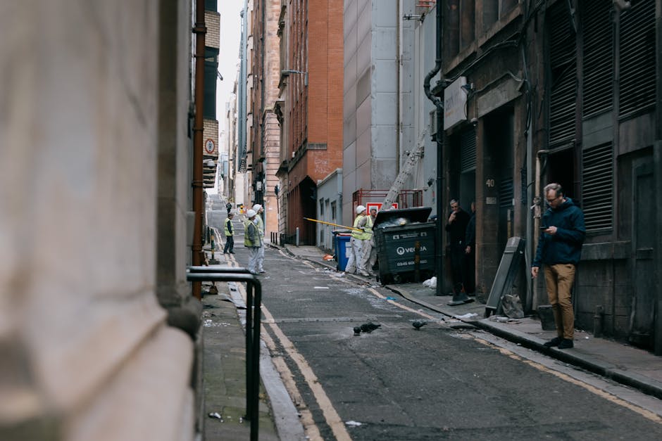 Photograph of a narrow external staircase made of dark stone, leading up to the entrance of a historic Glasgow tenement building with a stone facade. The staircase has a curved stone balustrade on one